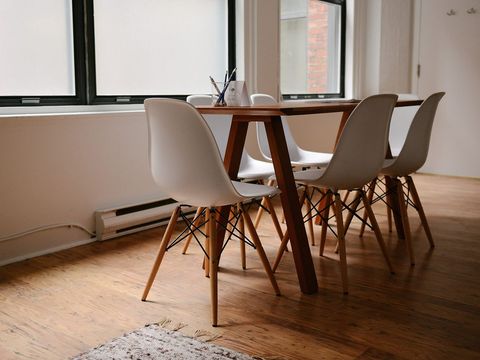 Leerer Besprechungsraum mit Holztisch, weißen Schalenstühlen und hellen Fenstern