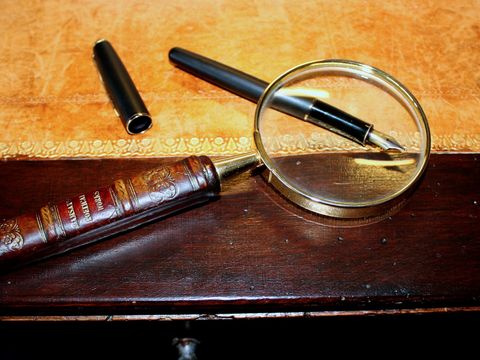 Lupe mit Messinggriff neben einem Füllfederhalter auf einem alten Schreibtisch