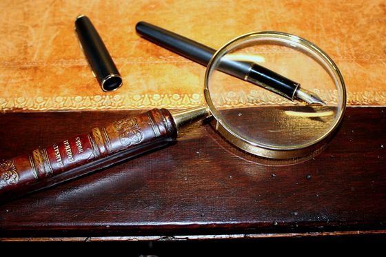 Lupe mit Messinggriff neben einem Füllfederhalter auf einem alten Schreibtisch