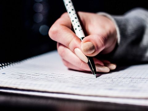 Hand schreibt mit Kugelschreiber Notizen in ein kariertes Spiralheft