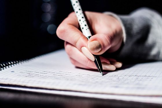 Hand schreibt mit Kugelschreiber Notizen in ein kariertes Spiralheft