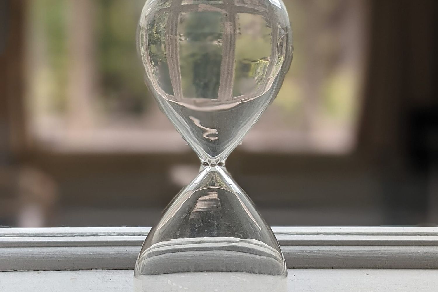 Gläserne Sanduhr mit dunklem Sand auf einer weißen Fensterbank