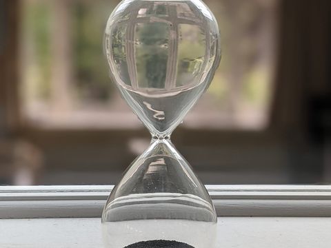Gläserne Sanduhr mit dunklem Sand auf einer weißen Fensterbank