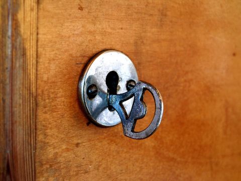 Alter Schlüssel steckt in einem Schlüsselloch mit Metallblende in einer Holztür