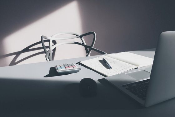 Taschenrechner, aufgeschlagenes Notizbuch mit Stift und Laptop auf einem hellen Schreibtisch