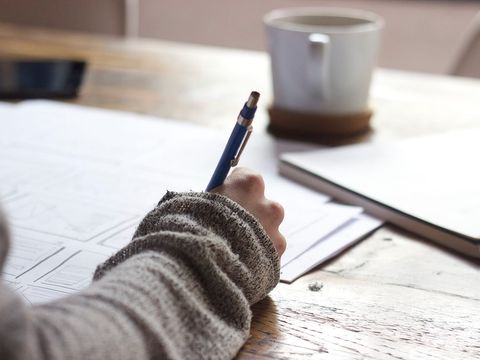 Hand skizziert mit Druckbleistift Website-Wireframes auf Papier, daneben Kaffeetasse und Notizbuch